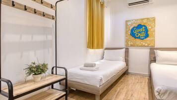 Une chambre d’hôtel avec deux lits, une petite table avec une plante, un climatiseur fixé au mur et un panneau indiquant « Sweet Chill Events ».