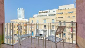 A balcony with two chairs and a small table, overlooking a cityscape with various buildings.
