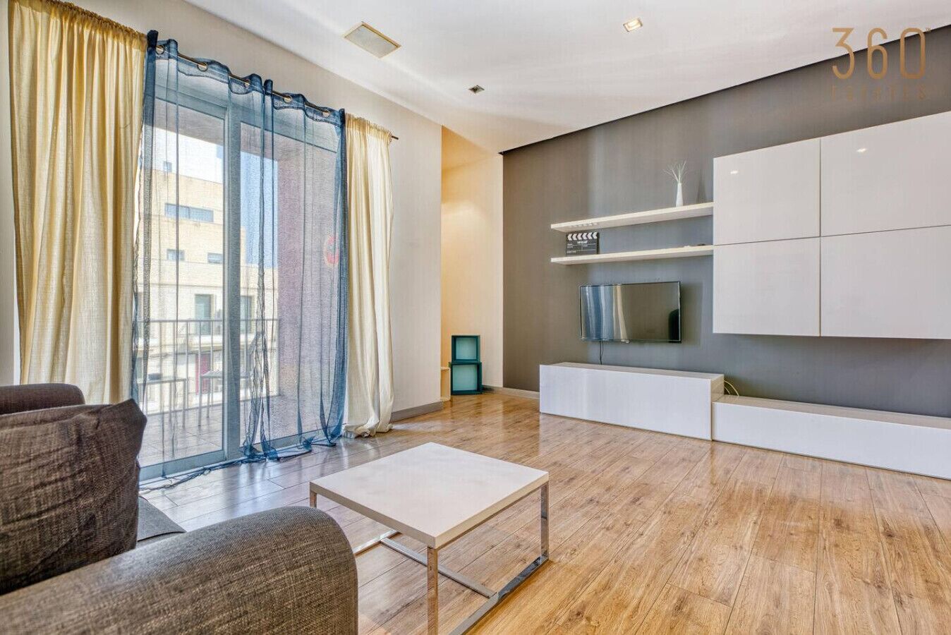 A modern living room with a sofa, a coffee table, and a TV mounted on a wall.