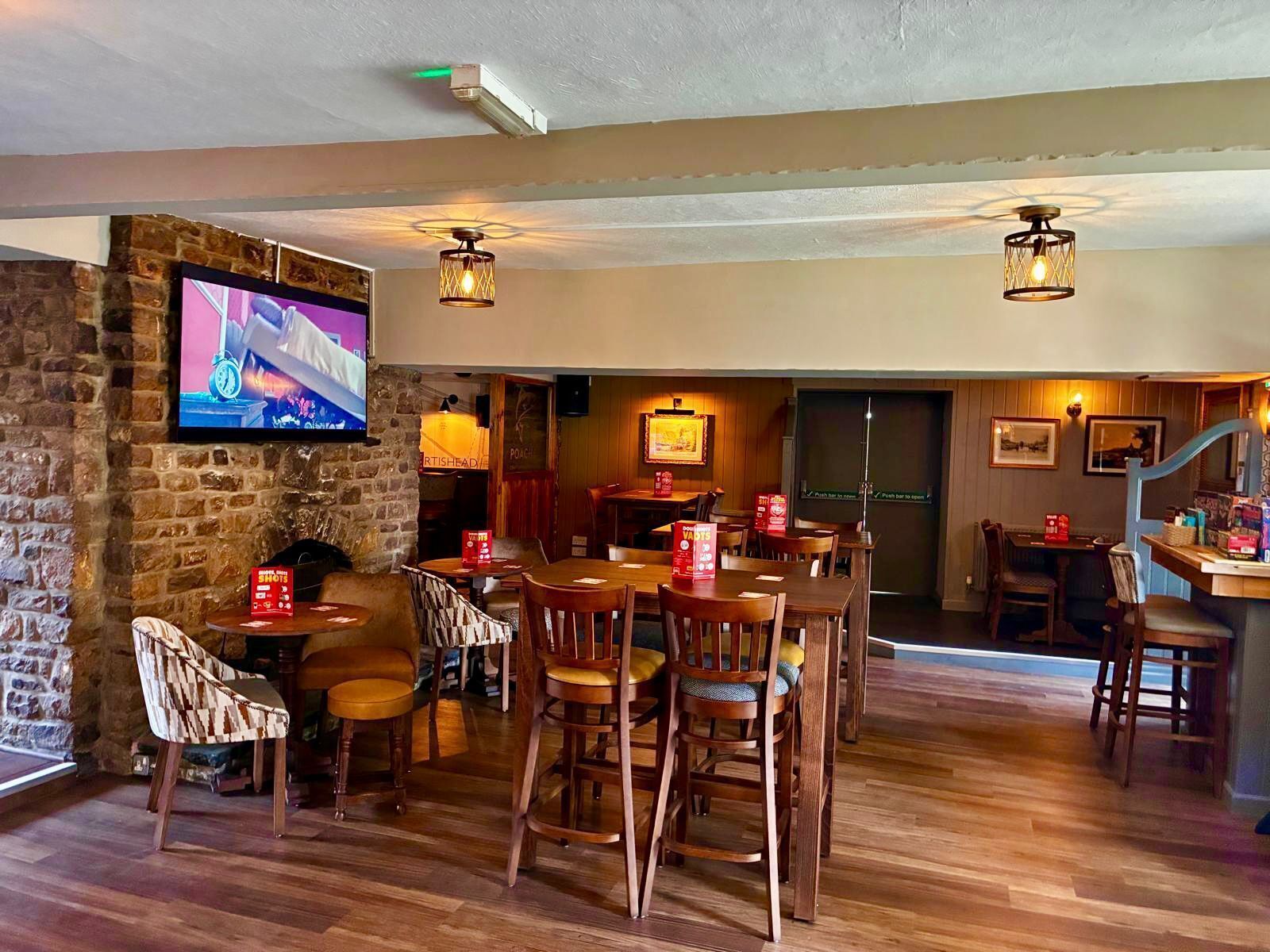 A restaurant with wooden furniture, a stone wall, and a television mounted on the wall.