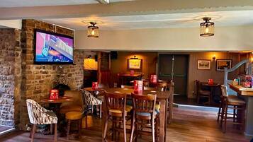 A restaurant with wooden furniture, a stone wall, and a television mounted on the wall.