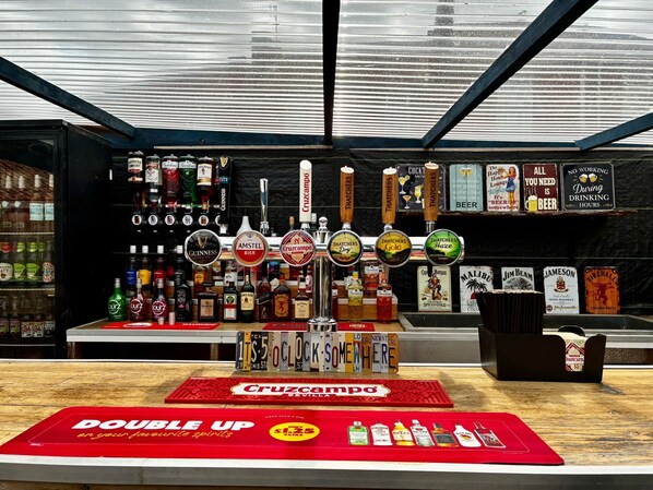Un bar con múltiples grifos de cerveza, una variedad de botellas de licor y un tapete rojo con la inscripción "DOUBLE UP" y "en tus licores favoritos".