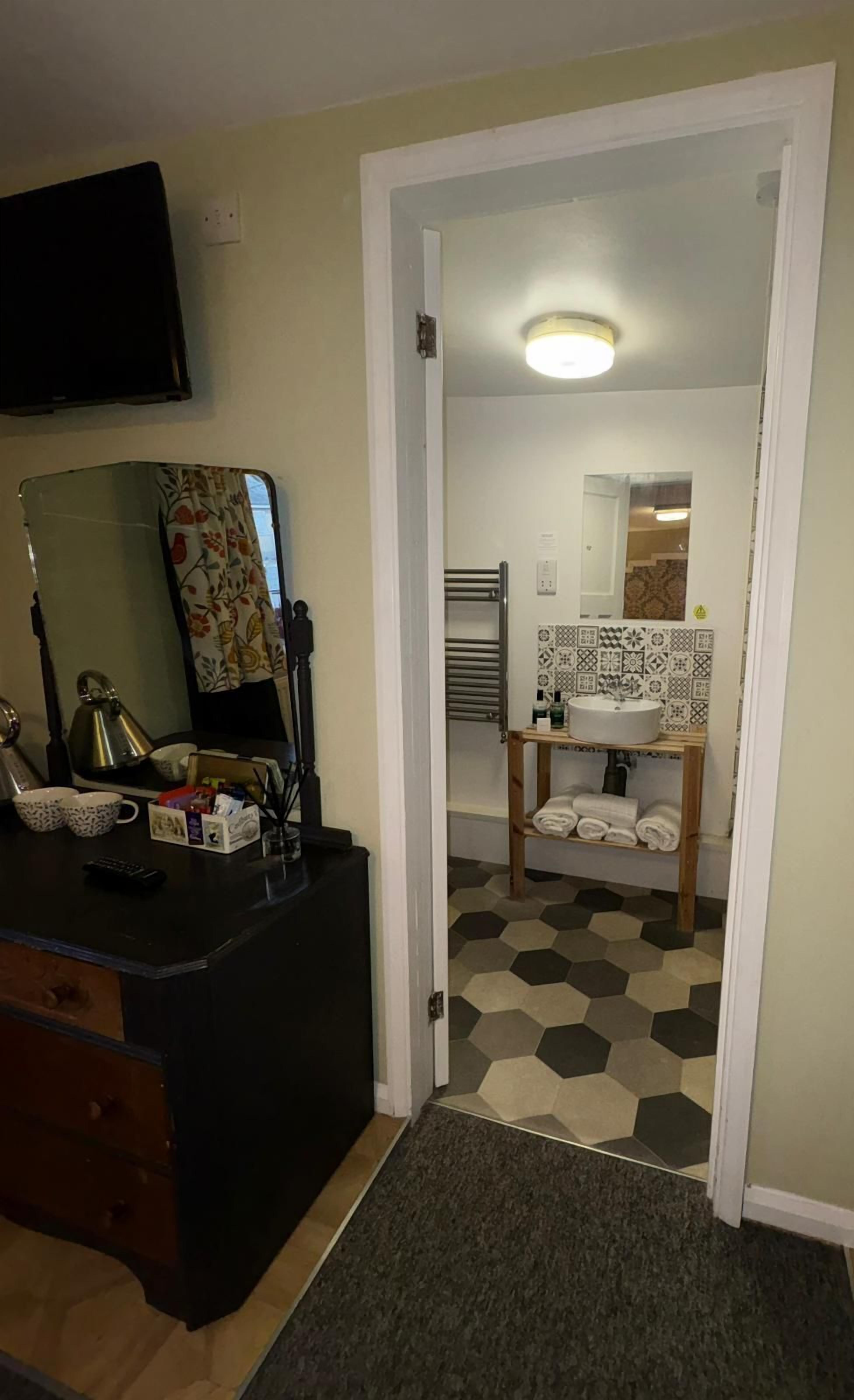 Une chambre dotée d’un bureau, d’un miroir et d’une salle de bain carrelée avec un lavabo.