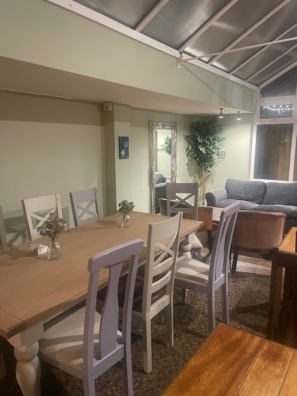 Un comedor con una mesa de madera y sillas blancas, un espejo y una planta en maceta.