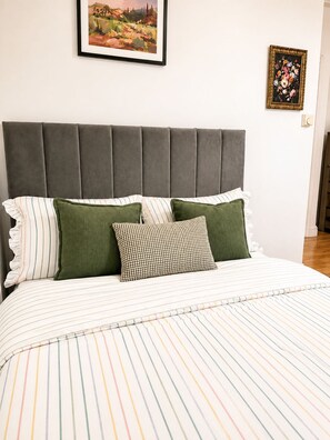 A bed with striped bedding, a grey upholstered headboard, and two pillows. - The Cozy Settle Stay - Relax and Unwind, 2 bedroom apartment near central London (London)