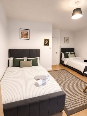 A hotel room with a large bed, a smaller bed, a patterned rug, and artwork on the walls. - The Cozy Settle Stay - Relax and Unwind, 2 bedroom apartment near central London (London)