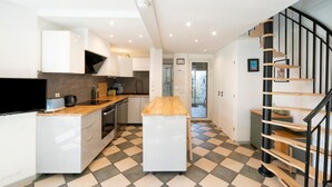 Una cocina moderna con una isla central, horno empotrado y televisor negro.