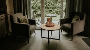 A room with two armchairs, a small round table with a tray of items, and a view of greenery outside. - Luxury Holiday Loft in Si-es-an (Balkbrug)