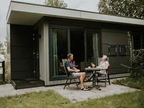 A modern outdoor seating area with a glass door entrance, a small table, and chairs. - Luxury Holiday Loft in Si-es-an (Balkbrug)