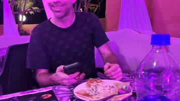 A person seated at a table with a menu, a plate of food, and a bottle.