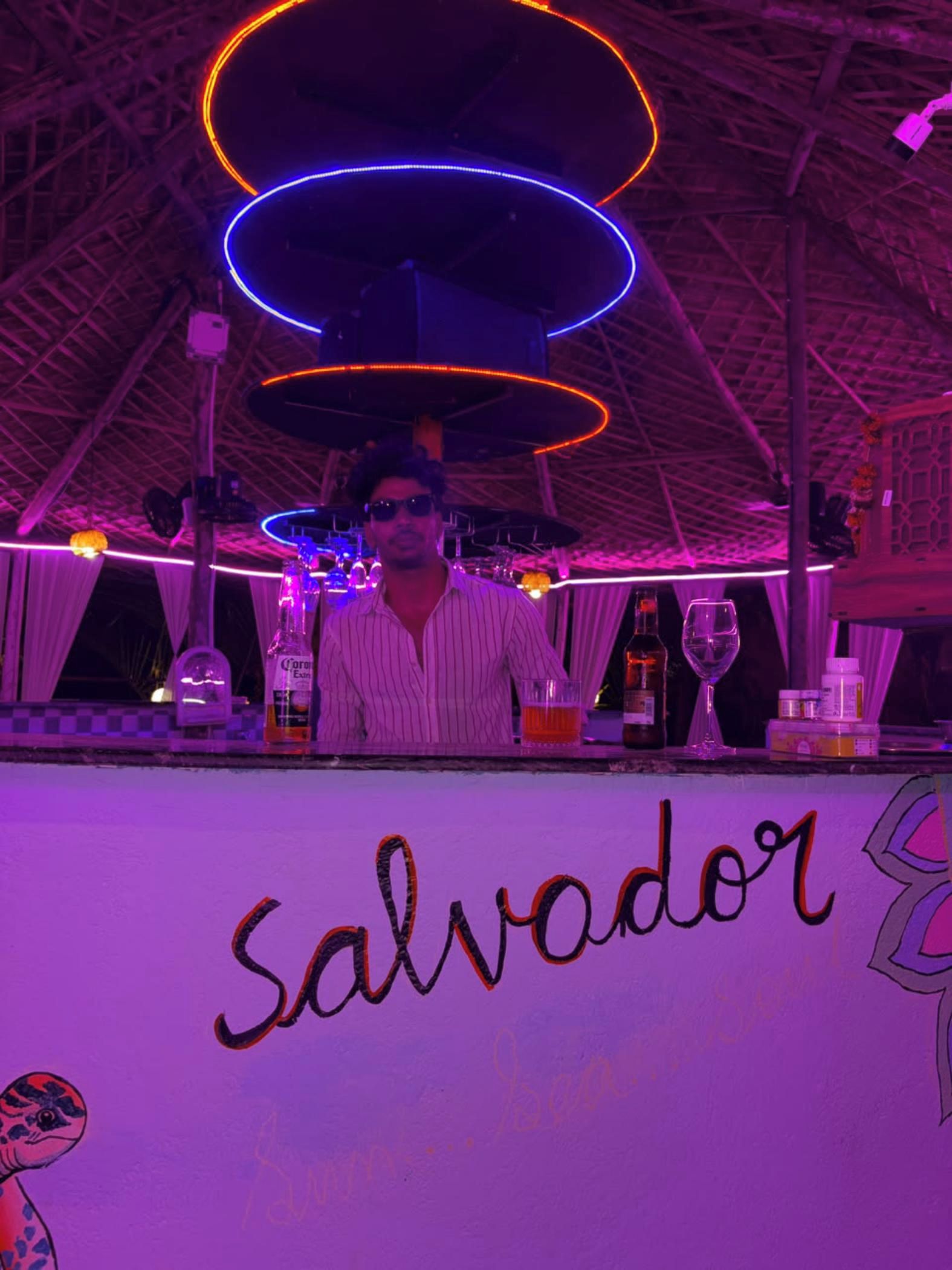 A bar area with a sign reading 'Salvador' and various bottles and glasses on the counter.