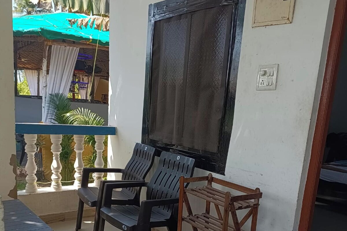 A room with a balcony, a table, two chairs, a wooden shelf, and a trash bin.