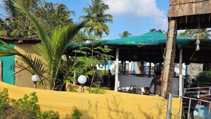 A rustic outdoor seating area with a covered structure, surrounded by greenery and palm trees. - Wood Castle Arambol (Arambol)