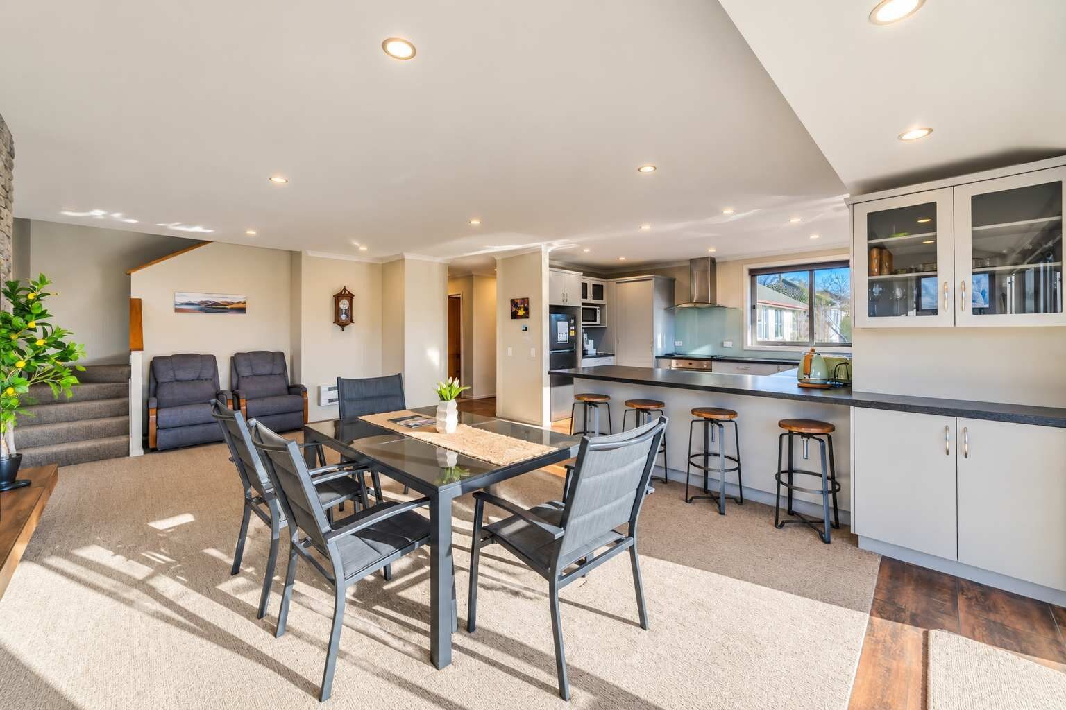 A modern kitchen with a central island, bar stools, and a dining area with a glass table and chairs.