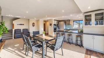 A modern kitchen with a central island, bar stools, and a dining area with a glass table and chairs.