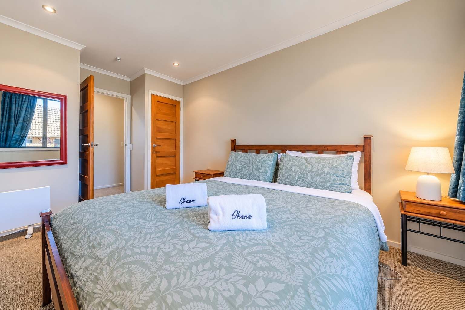 A hotel room with a large bed, two pillows, a bedside table with a lamp, and a window with curtains.