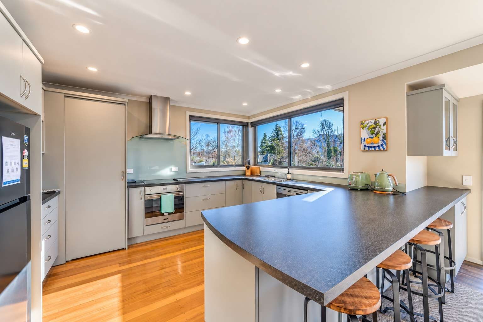 A modern kitchen with a large island, built-in oven, and a view through the windows.