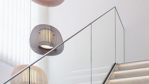 Una escalera moderna con barandilla de vidrio y tres lámparas colgantes de diseño acanalado.