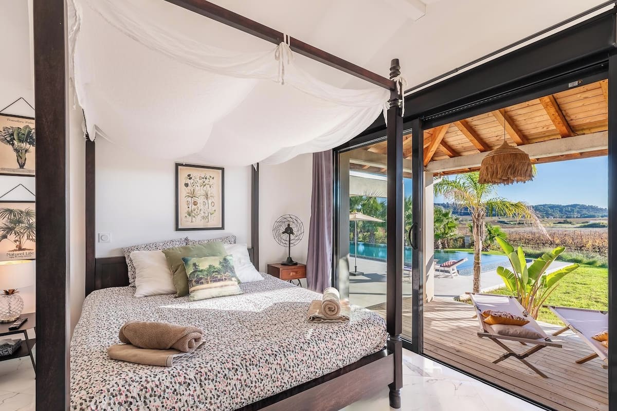 Un dormitorio con cama a dosel, vista a una piscina y terraza de madera afuera.
