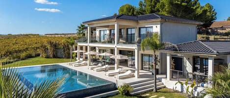A modern two-story house with a swimming pool, outdoor seating, and a view of the surrounding landscape.