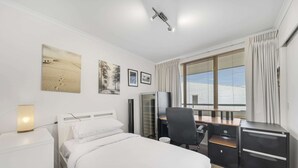A modern hotel room with a bed, desk, chair, and a large window with curtains. - Bright 2-bed With Private Balcony (Canberra)