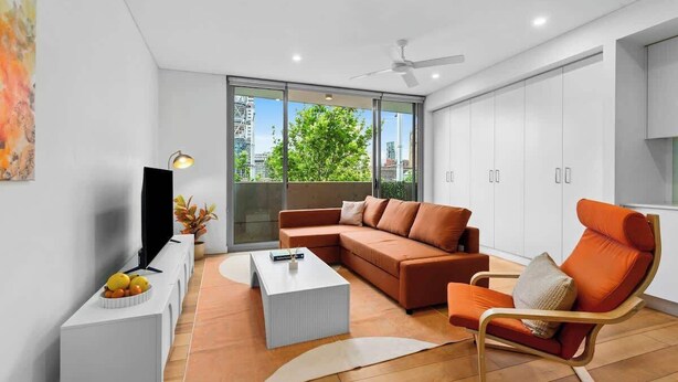 A modern living room with a sectional sofa, a coffee table, and a TV on a stand. - Central Art-filled 2 Beds With Balcony Aircon (Sydney)