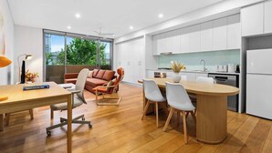 A modern kitchen with white cabinets, a central island, and a dining area with chairs. - Central Art-filled 2 Beds With Balcony Aircon (Sydney)
