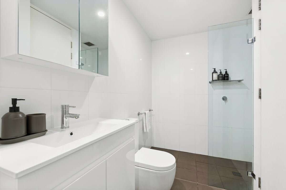 A modern bathroom with a white vanity, a glass shower enclosure, and a white toilet.