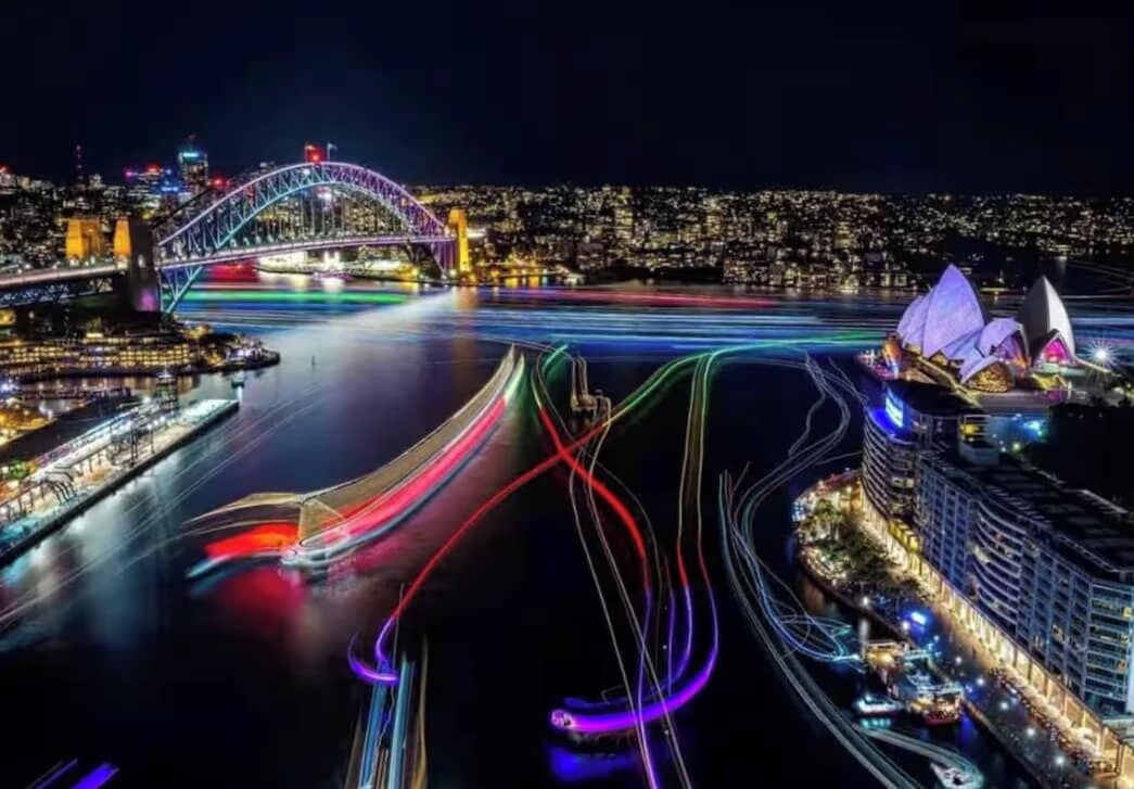 A nighttime cityscape with a prominent bridge and the Sydney Opera House.