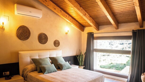 A bedroom with a bed, bedside tables, a wall-mounted air conditioner, and a window with curtains. - Cal Vientos (Paüls)