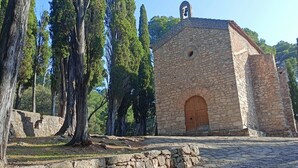 A stone building with a wooden door and a small bell tower, surrounded by trees. - Cal Vientos (Paüls)