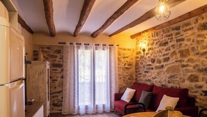 A cozy room with a stone wall, wooden beams, a red sofa, and a wooden table with a woven basket. - Cal Vientos (Paüls)