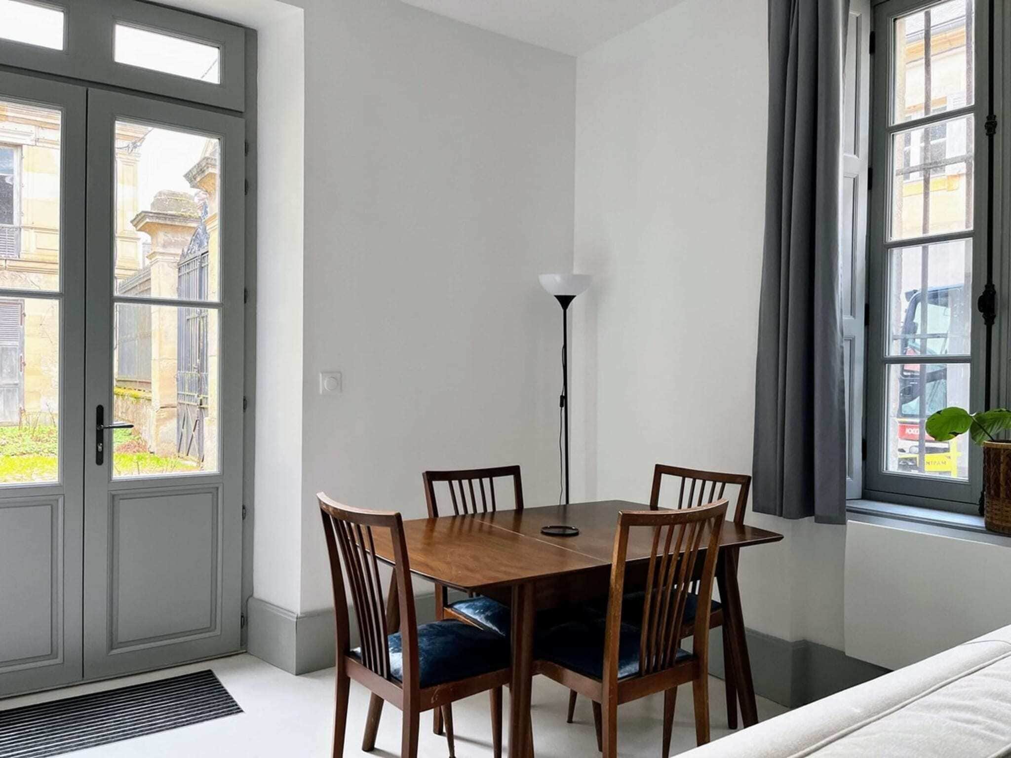 A dining area with a wooden table and chairs, a floor lamp, and a view through large windows.