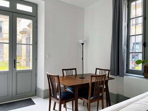 A dining area with a wooden table and chairs, a floor lamp, and a view through large windows. - Maison Constant - The Redwood (Autun)