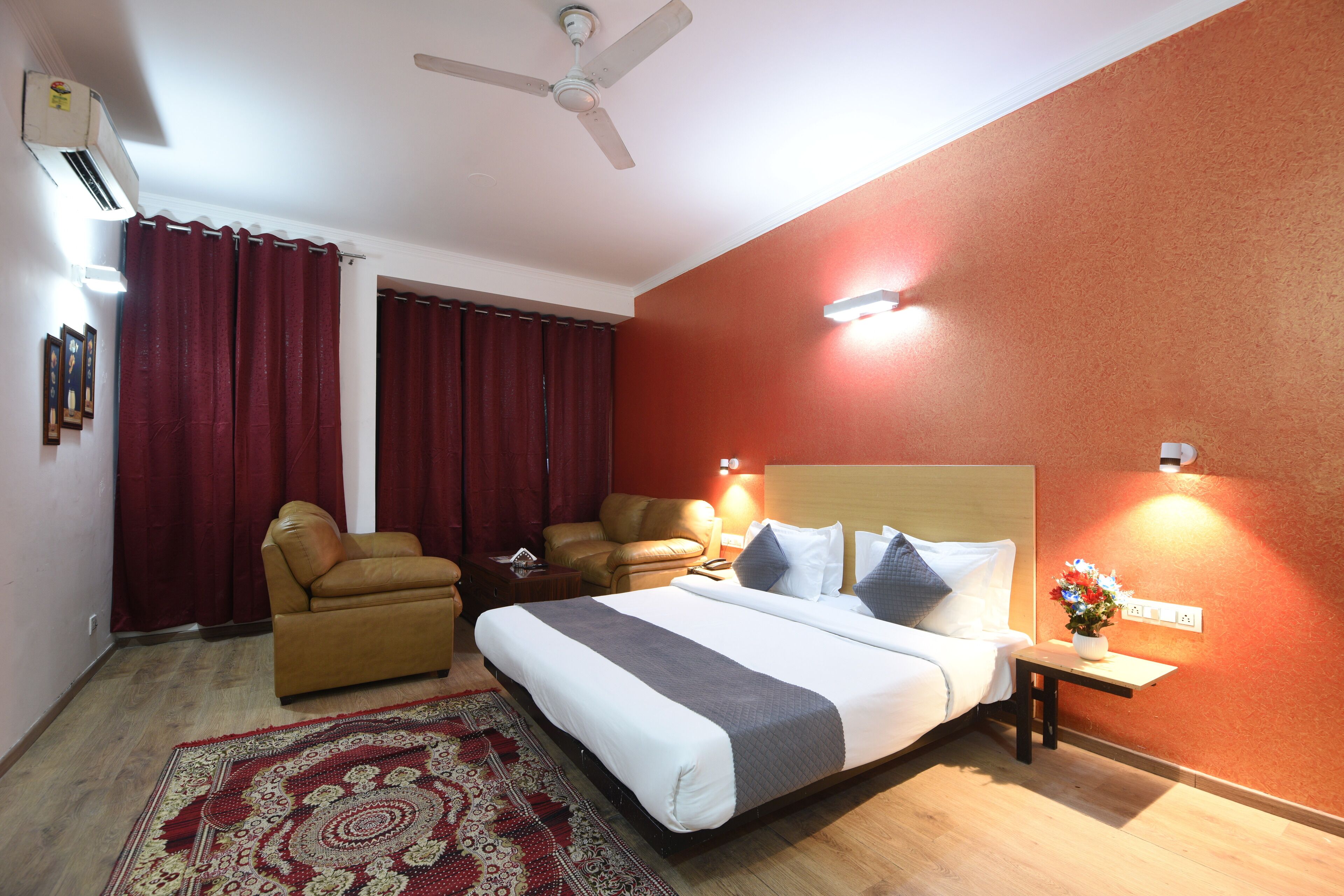 Une chambre d’hôtel avec un lit, deux chaises, une petite table avec un vase et un ventilateur de plafond.