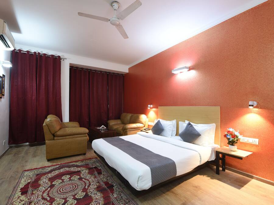Une chambre d’hôtel avec un lit, deux chaises, une petite table avec un vase et un ventilateur de plafond.