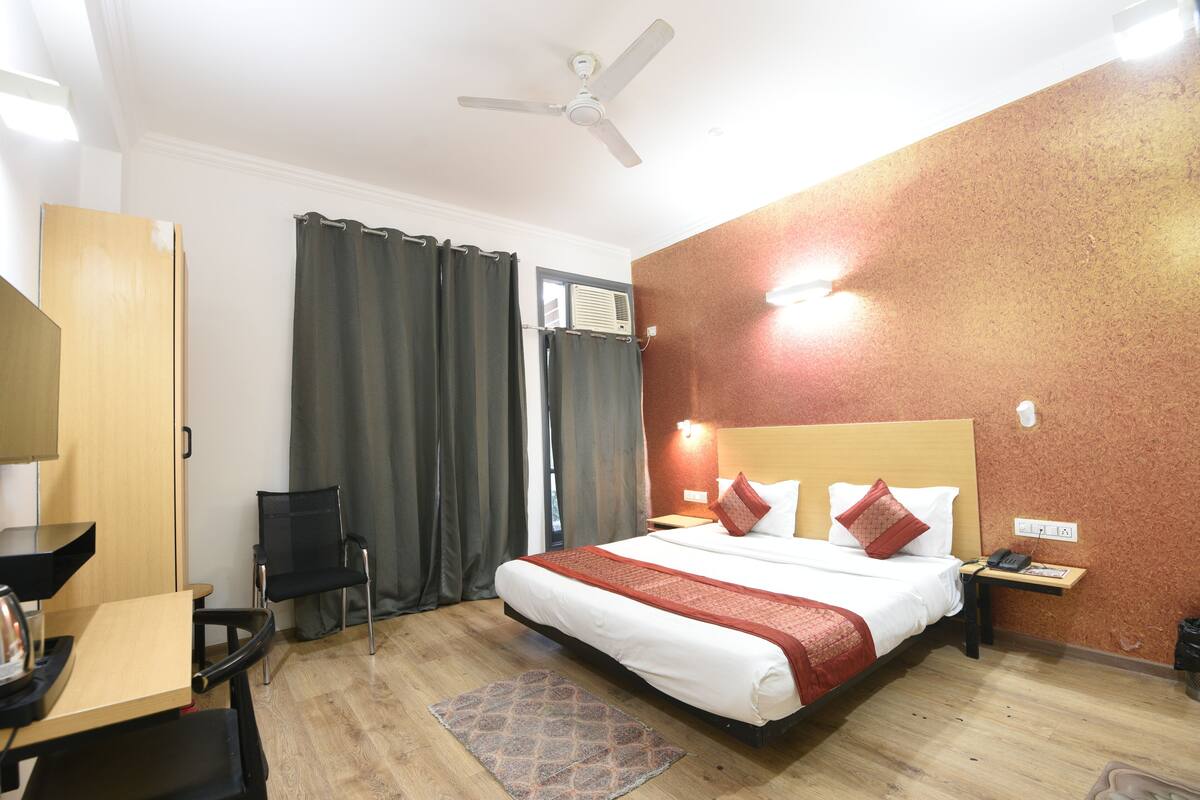 Een hotelkamer met een bed, een bureau, een stoel, een plafondventilator en een raam met gordijnen.