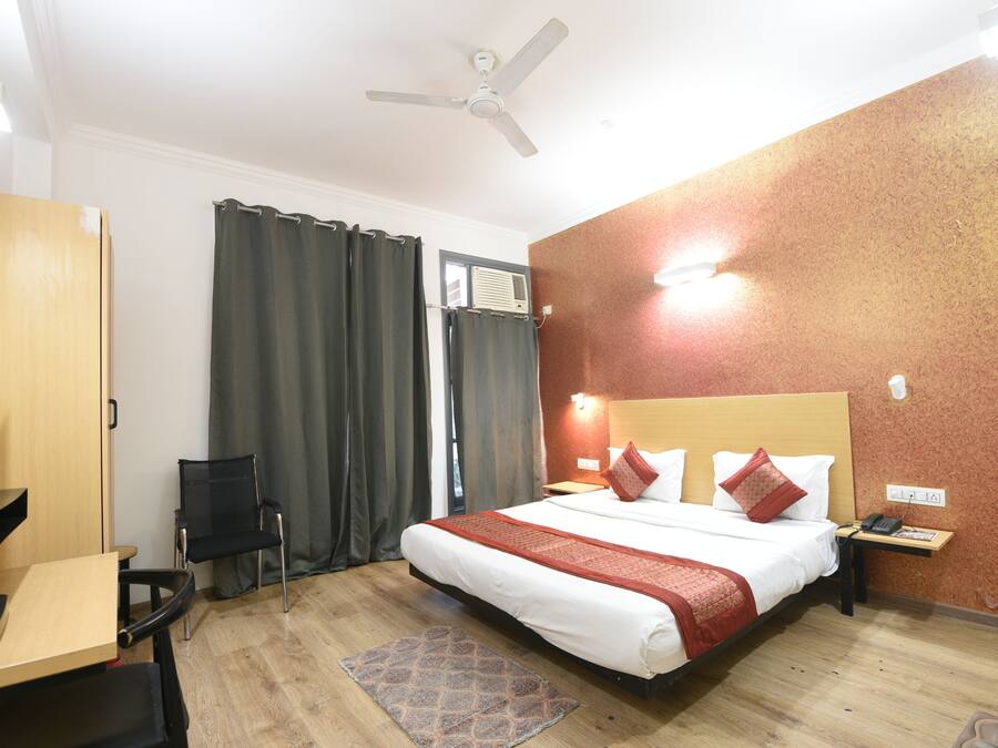 Habitación de hotel con cama, escritorio, silla, ventilador de techo y ventana con cortinas.