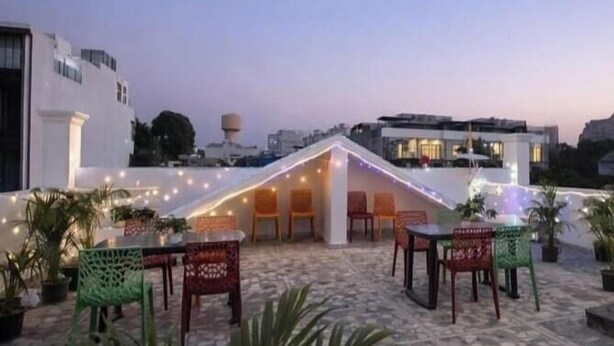 A rooftop terrace with tables and chairs, string lights, and potted plants. - royal spark inn03 (Gurugram)