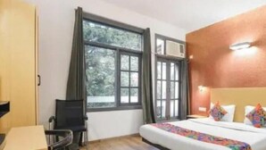 A hotel room with a bed, a desk, a chair, and a window with curtains. - royal spark inn03 (Gurugram)