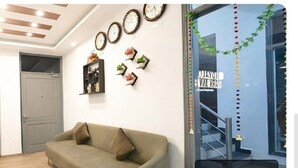 A room with a sofa, two doors, wall clocks, and a window with a view of a staircase. - royal spark inn03 (Gurugram)