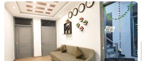 Una habitación con sofá, dos puertas, relojes de pared y una ventana con vista a una escalera.