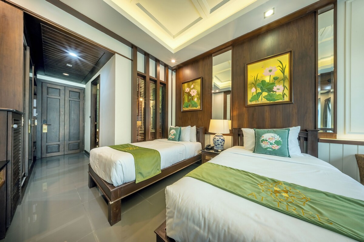 A hotel room with two beds, a wooden wardrobe, a mirror, and a painting.
