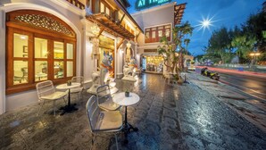 An outdoor seating area with tables and chairs, a sign reading 'At Tree Hotel,' and a street with a motorcycle parked on the side. - At Tree Hotel Thaphae Gate Chiangmai (Chiang Mai)