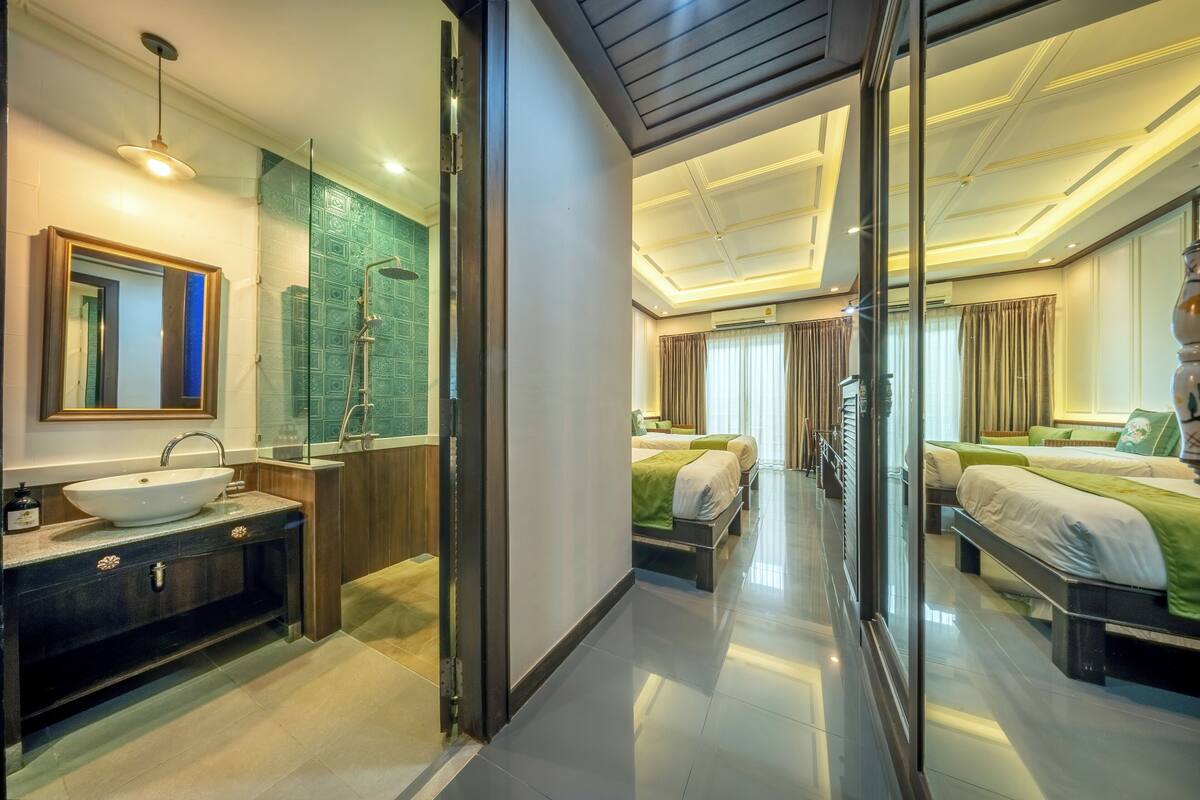 Une chambre d’hôtel moderne, dotée d’un grand miroir, d’un lavabo, d’une douche et de deux lits avec une literie verte.