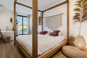 Une chambre avec un grand lit, une vue sur l’extérieur, une baignoire et une décoration murale en macramé.
