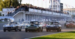 Carros de corrida antigos numa pista, com espectadores ao fundo.