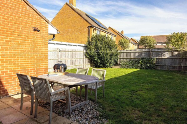A patio with a table and chairs, a barbecue grill, and a wooden fence in a residential backyard. - Coastal Home for 6 in The Witterings (Chichester)