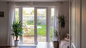 Une pièce dotée d’une porte-fenêtre coulissante donnant sur un jardin, d’une table en bois et de deux plantes en pot.