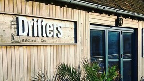 Un bâtiment en bois sur lequel est apposée une enseigne indiquant : « Drifters Kitchen Bar ».